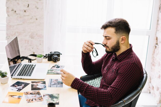 A man looks at photographs while sitting in the office in front of a laptop