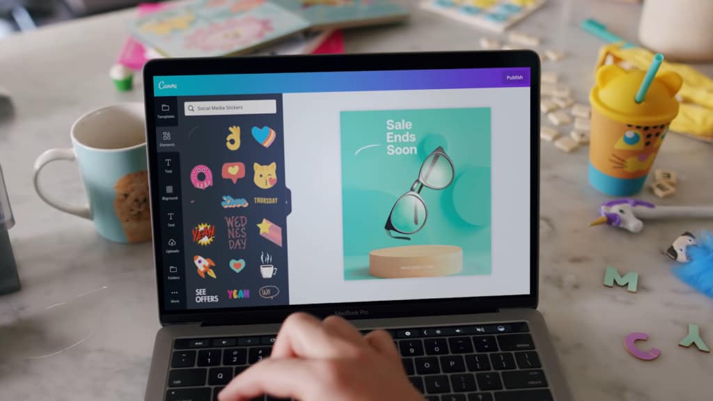 A Canva design on a laptop with a cookie and colorful items on the table